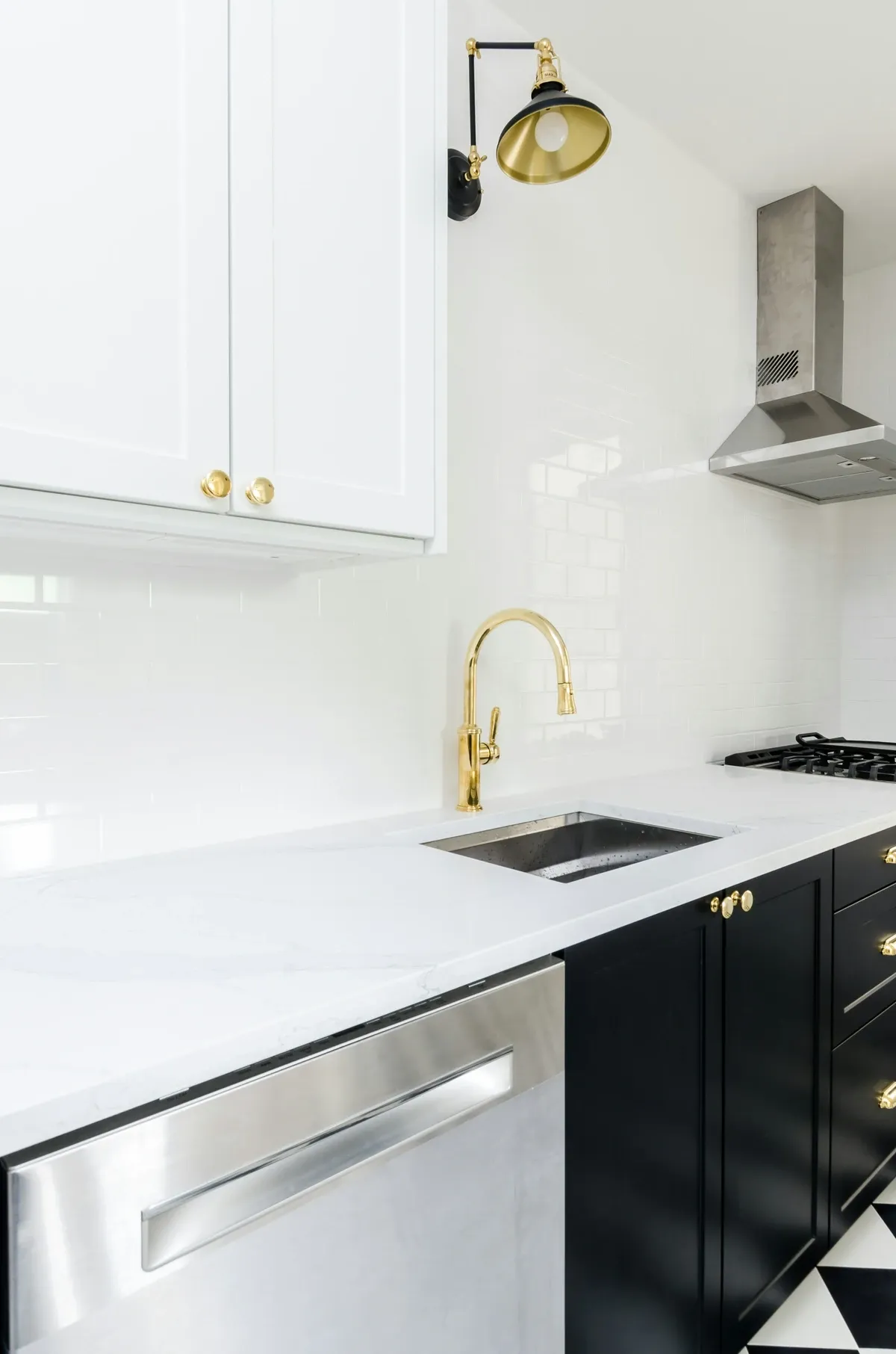 White kitchen with a brass faucet and a brass wall sconce above a white counter and black lower cabinets