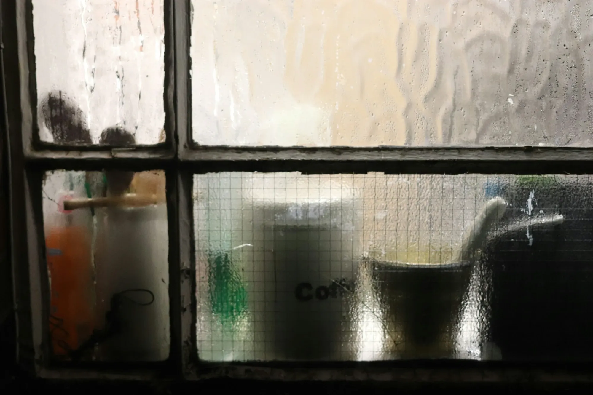 Coffee mugs and a canister seen through a frosted kitchen window pane in winter light