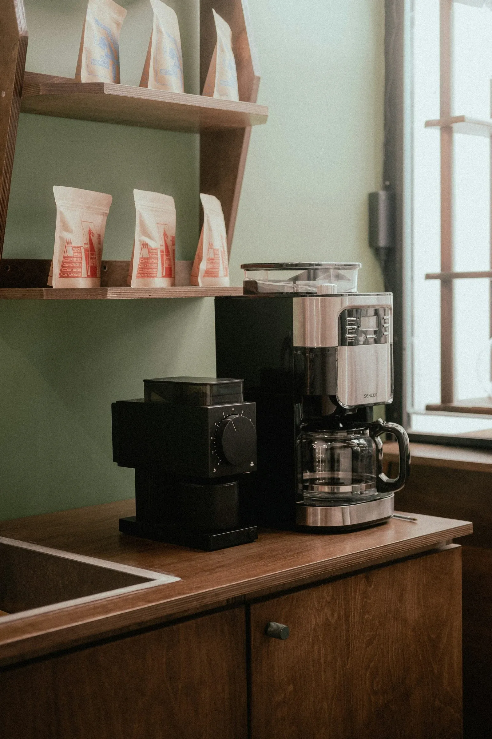 Warm wood coffee bar counter with a grinder against a green wall