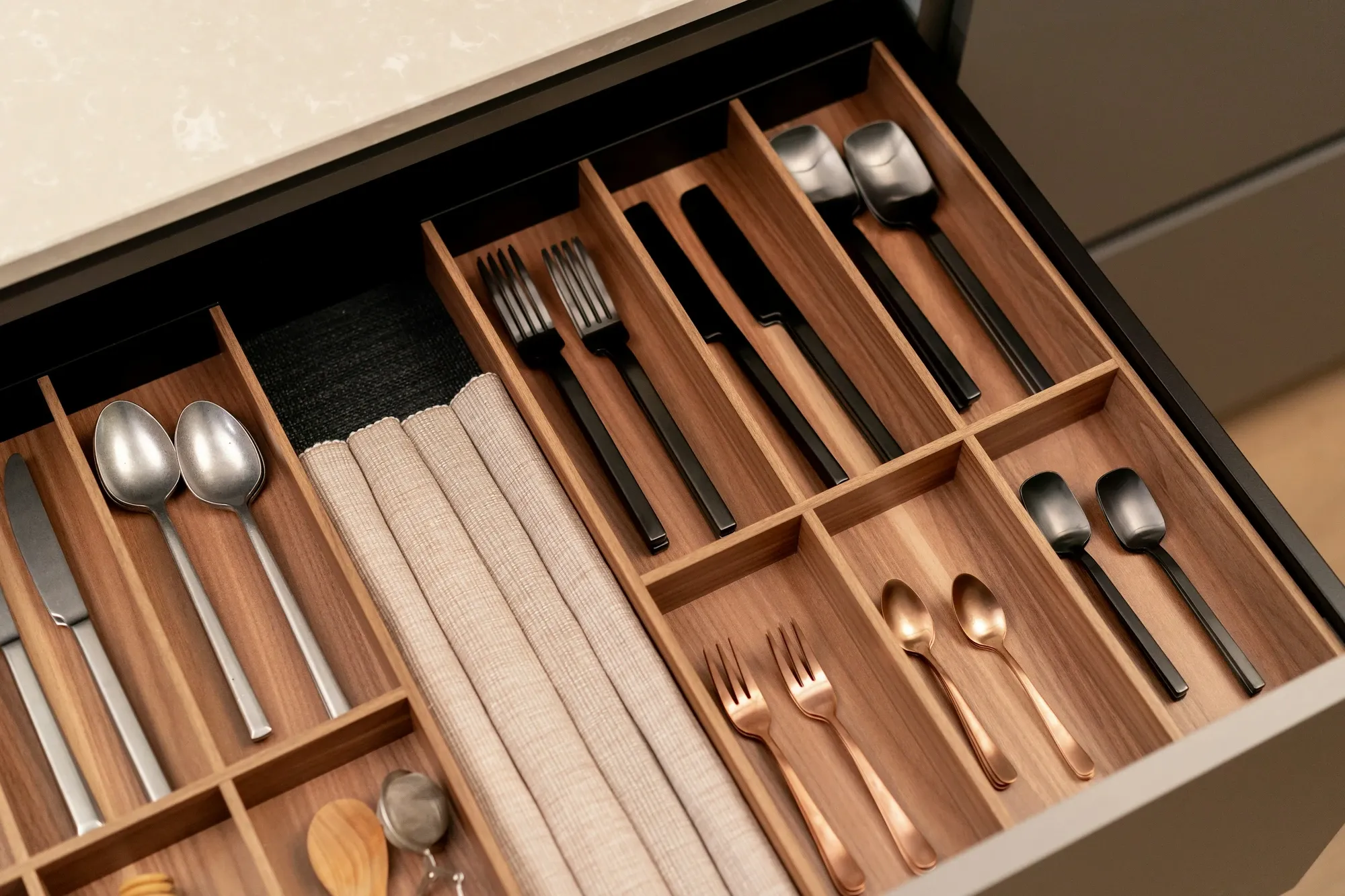 Kitchen drawer fitted with a wood divider organizer holding spoons, forks and folded linen napkins