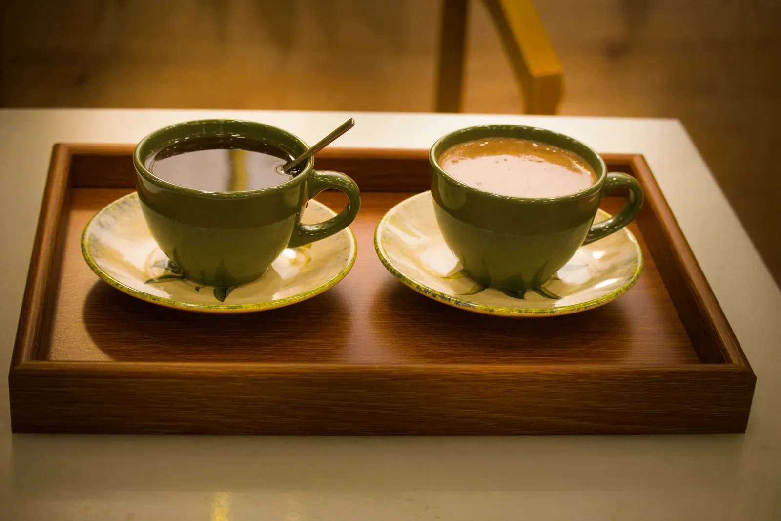 Wooden serving tray holding two cups of coffee on saucers on a table